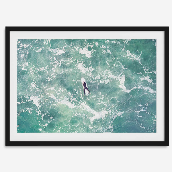 Fine art aerial photography print of a lone surfer floating on a surfboard amidst turquoise ocean waves with intricate white foam patterns.