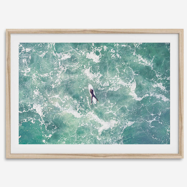 Fine art aerial photography print of a lone surfer floating on a surfboard amidst turquoise ocean waves with intricate white foam patterns.