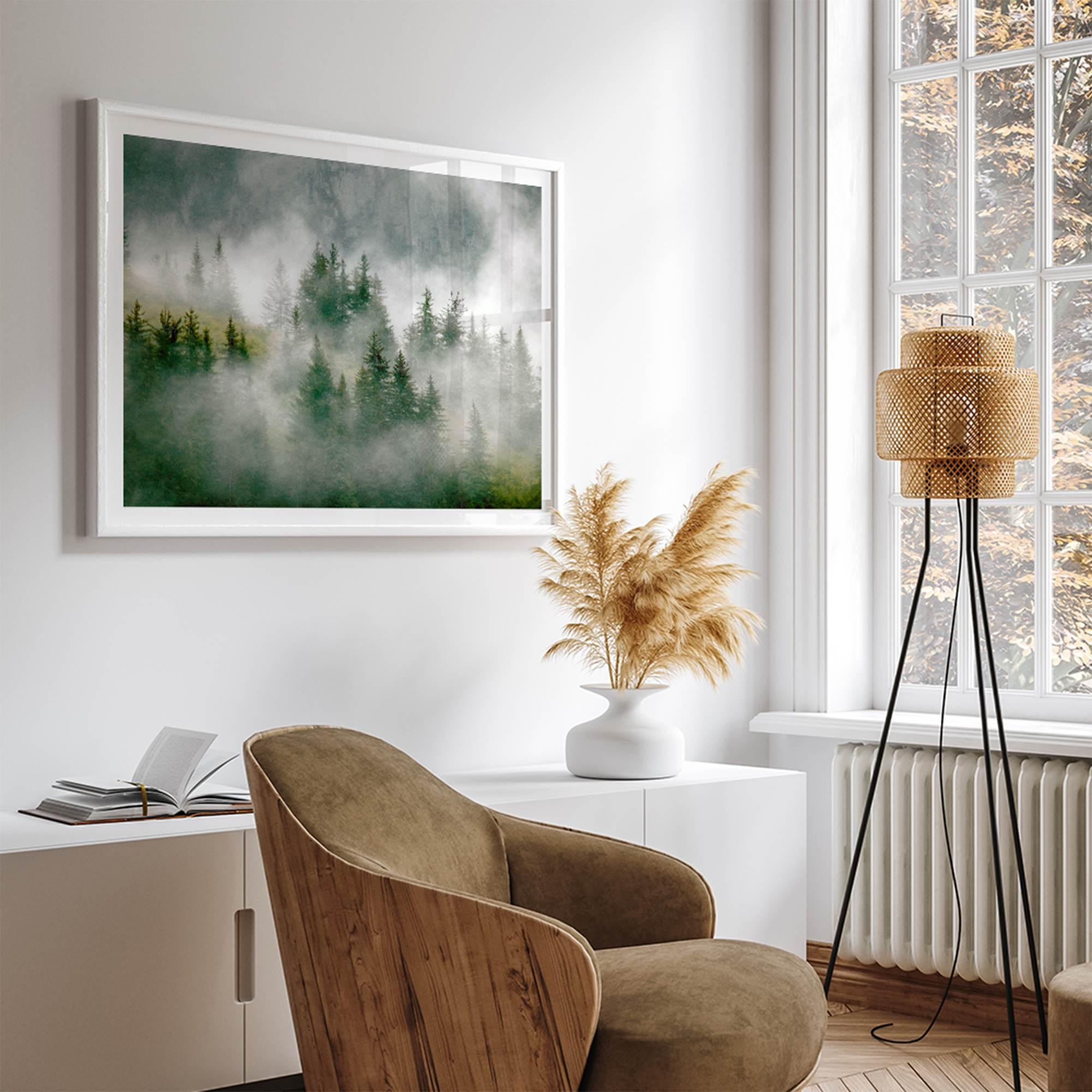 Fine art photography of a misty forest in Alaska, with the tops of trees on a mountain shrouded in white dreamlike fog.