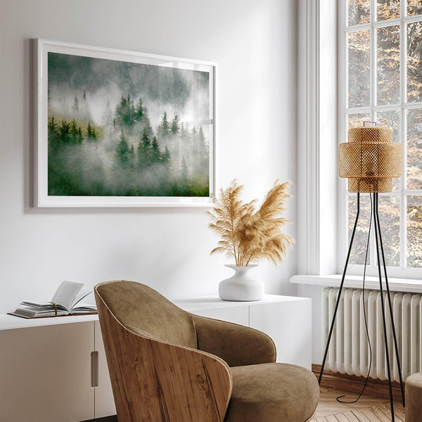 Fine art photography of a misty forest in Alaska, with the tops of trees on a mountain shrouded in white dreamlike fog.