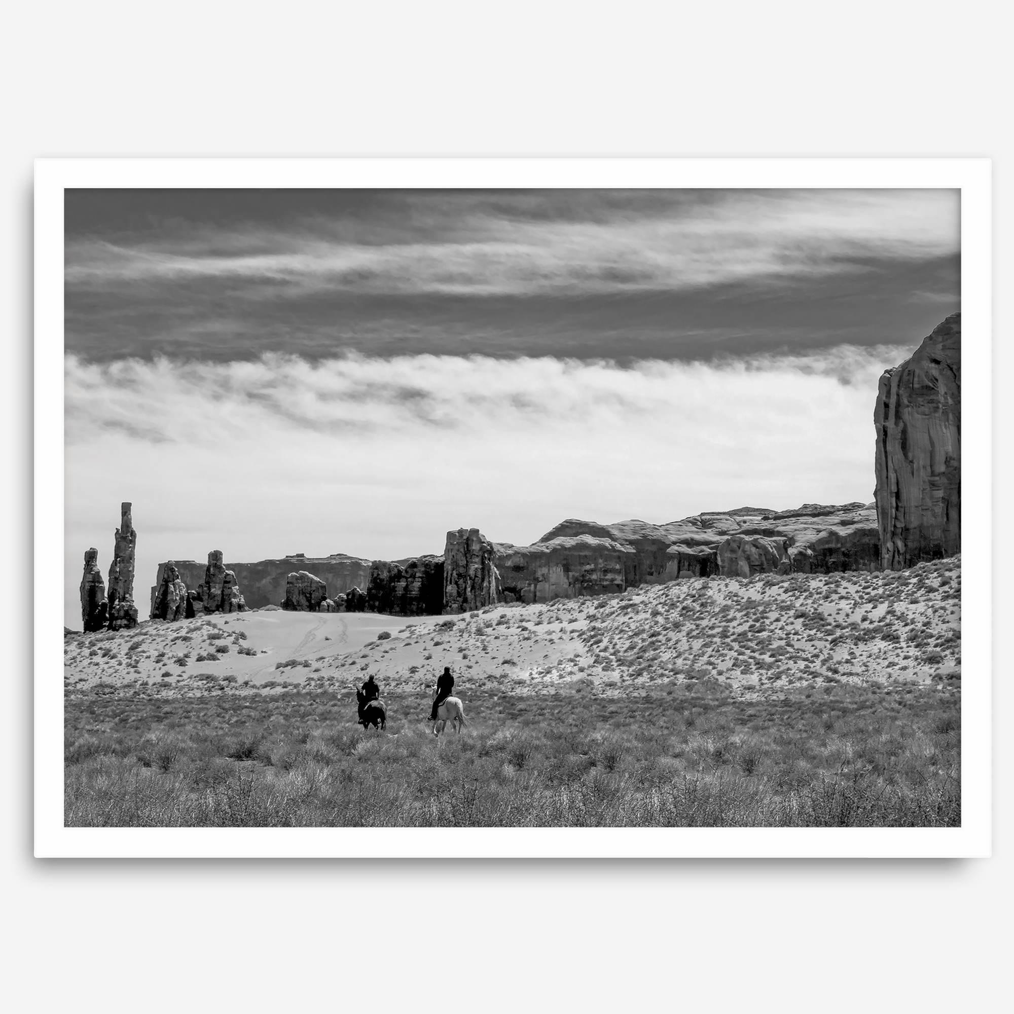 This Utah desert fine art photography print features two horse riders riding toward the horizon of the Utah desert with the unique towering rocks of Monument Valley as the backdrop. The dramatic cloudy sky adds intensity and beauty to the scene.