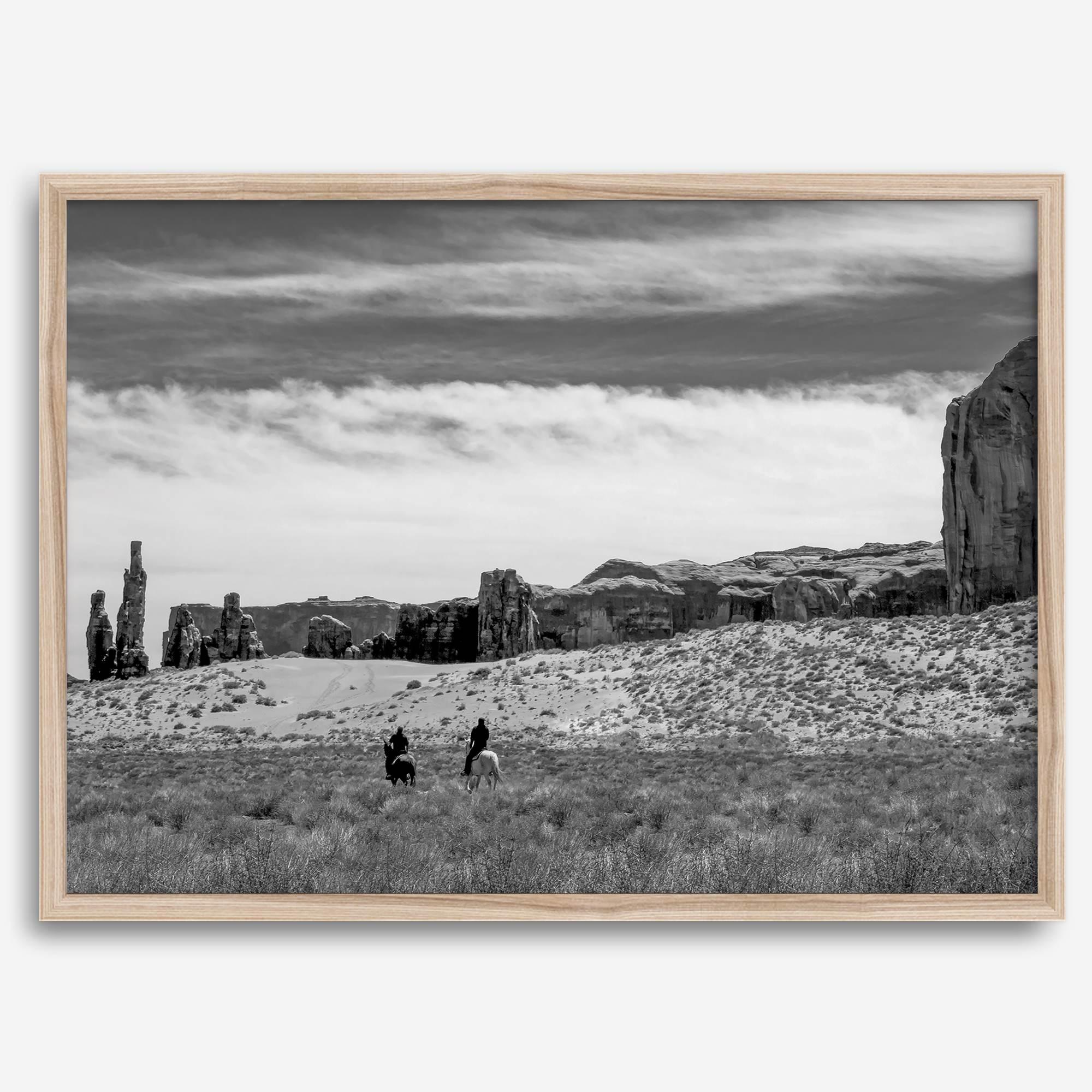 This Utah desert fine art photography print features two horse riders riding toward the horizon of the Utah desert with the unique towering rocks of Monument Valley as the backdrop. The dramatic cloudy sky adds intensity and beauty to the scene.