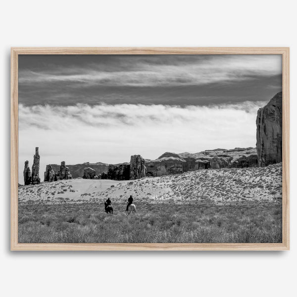 This Utah desert fine art photography print features two horse riders riding toward the horizon of the Utah desert with the unique towering rocks of Monument Valley as the backdrop. The dramatic cloudy sky adds intensity and beauty to the scene.