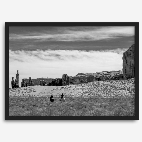 This Utah desert fine art photography print features two horse riders riding toward the horizon of the Utah desert with the unique towering rocks of Monument Valley as the backdrop. The dramatic cloudy sky adds intensity and beauty to the scene.