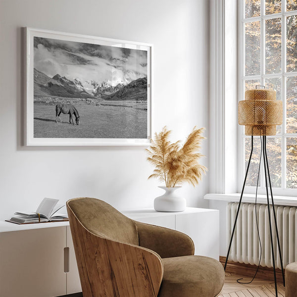 A black and white mountain horse fine art print that can come framed on unframed and was taken in Peru. This mountain wall art showcases snow-covered mountains in Peru and a charming horse grazing relaxingly in the forefront of the picture.