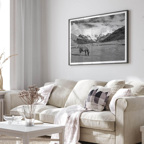 A black and white mountain horse fine art print that can come framed on unframed and was taken in Peru. This mountain wall art showcases snow-covered mountains in Peru and a charming horse grazing relaxingly in the forefront of the picture.