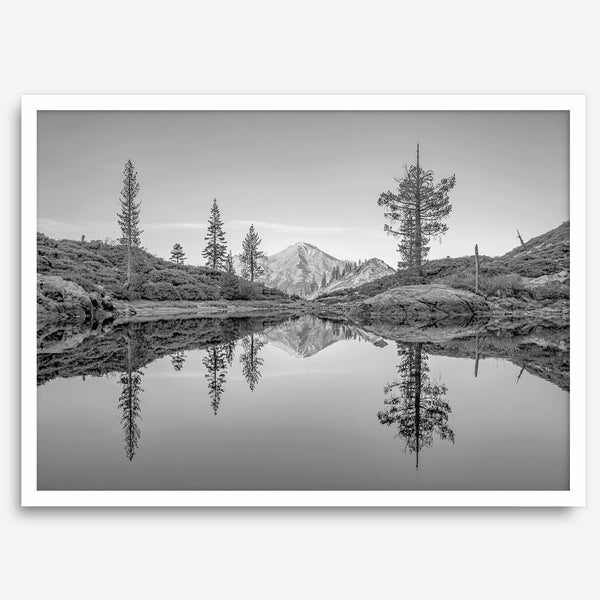 Black and white fine art photo of a serene mountain and forest mirrored in a still lake at sunset.