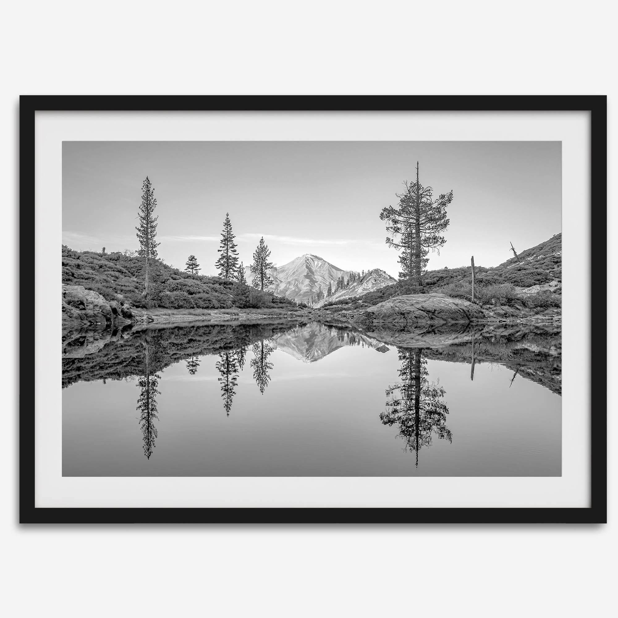 Black and white fine art photo of a serene mountain and forest mirrored in a still lake at sunset.