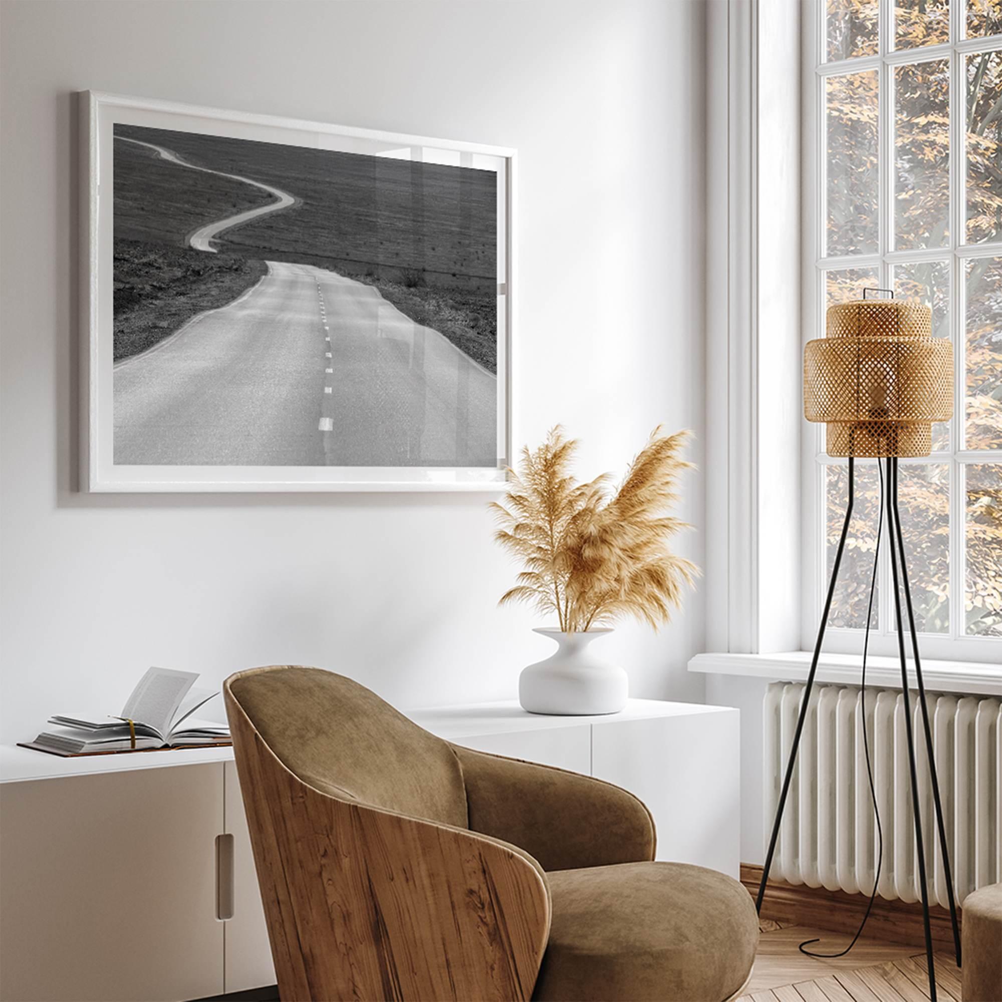 Black and white fine art photo of a winding desert road stretching through a vast minimalist landscape.