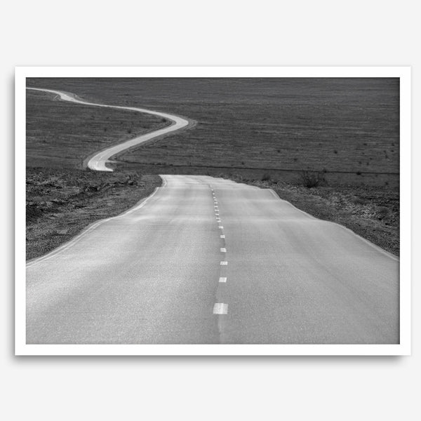 Black and white fine art photo of a winding desert road stretching through a vast minimalist landscape.