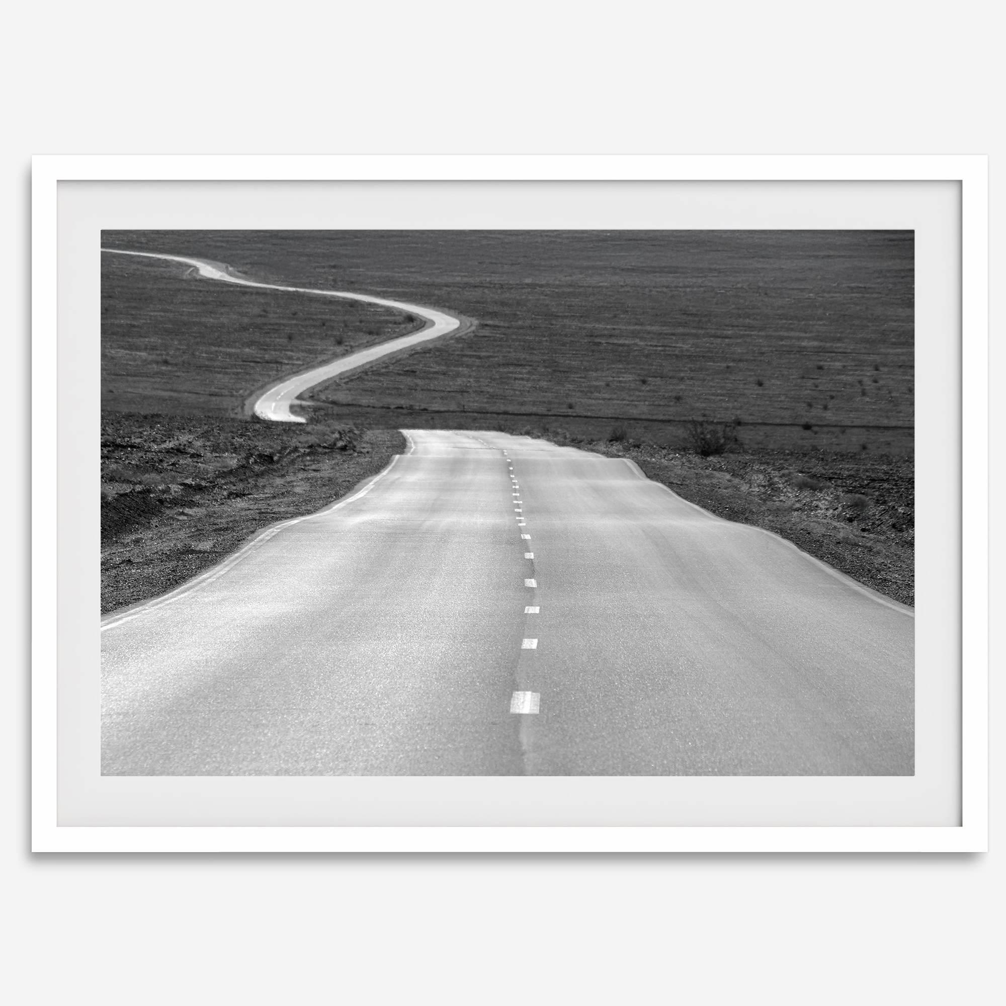 Black and white fine art photo of a winding desert road stretching through a vast minimalist landscape.