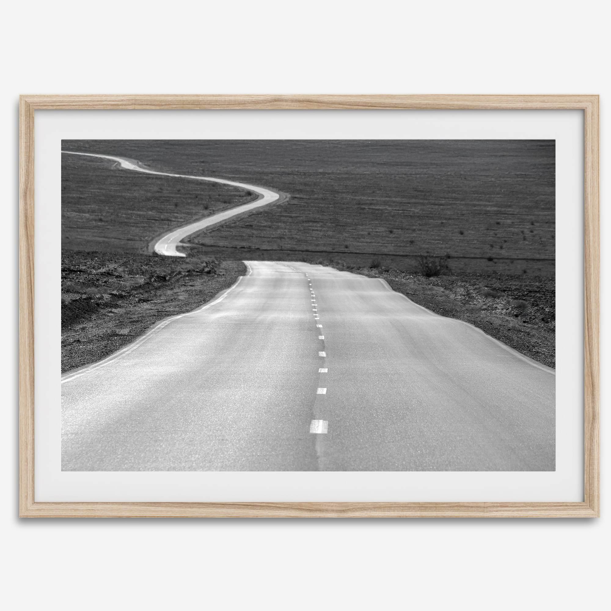Black and white fine art photo of a winding desert road stretching through a vast minimalist landscape.