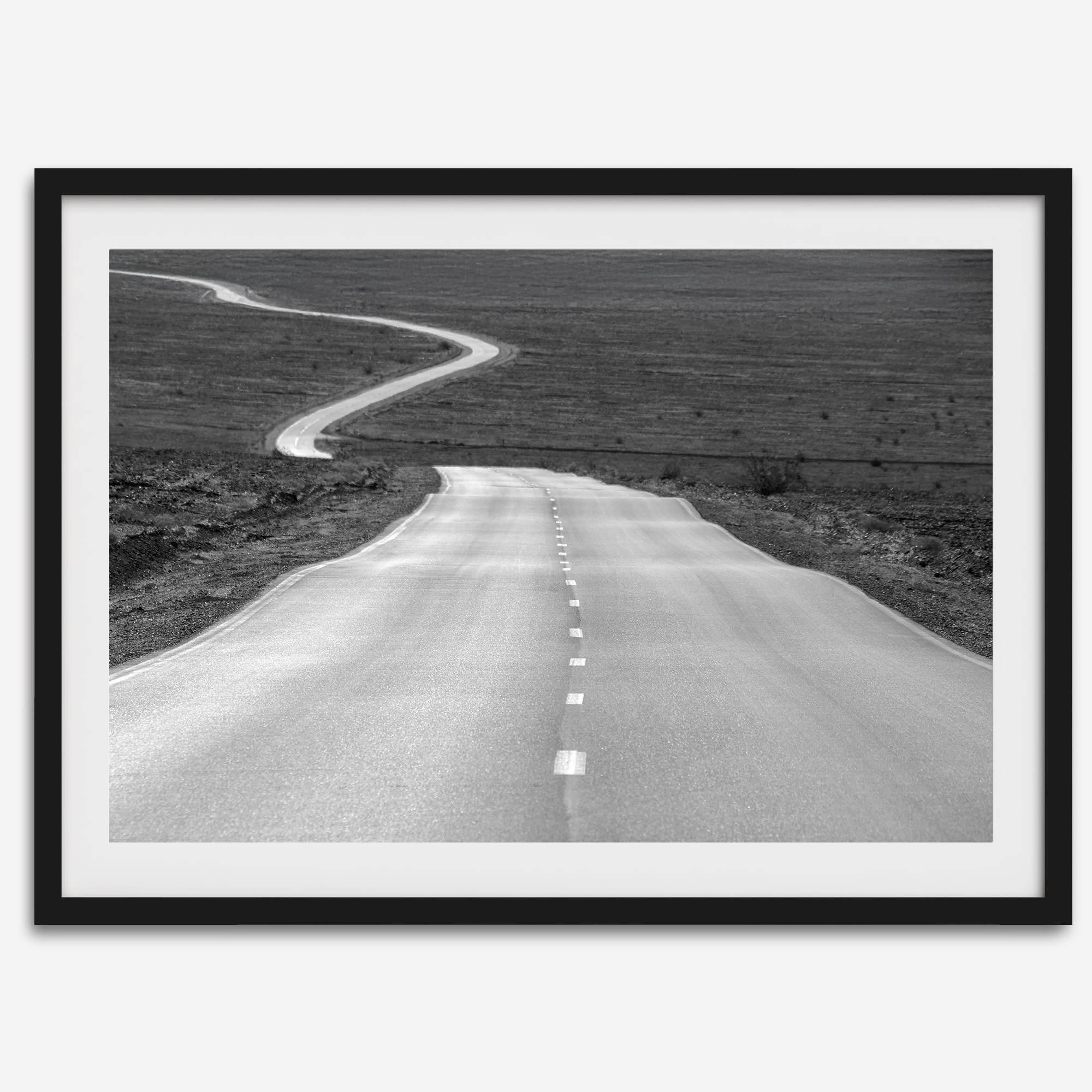 Black and white fine art photo of a winding desert road stretching through a vast minimalist landscape.