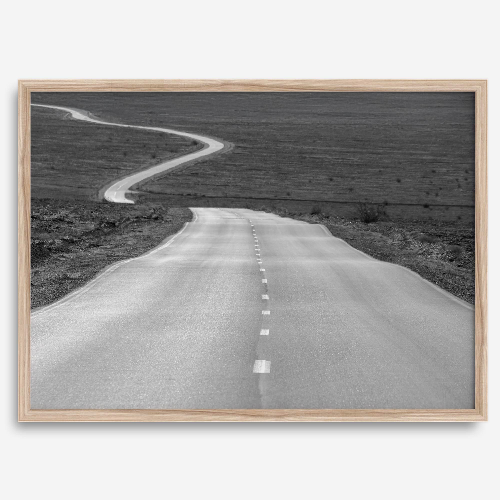 Black and white fine art photo of a winding desert road stretching through a vast minimalist landscape.