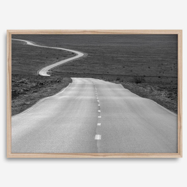 Black and white fine art photo of a winding desert road stretching through a vast minimalist landscape.