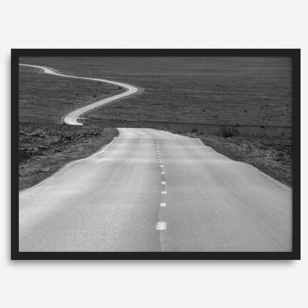 Black and white fine art photo of a winding desert road stretching through a vast minimalist landscape.