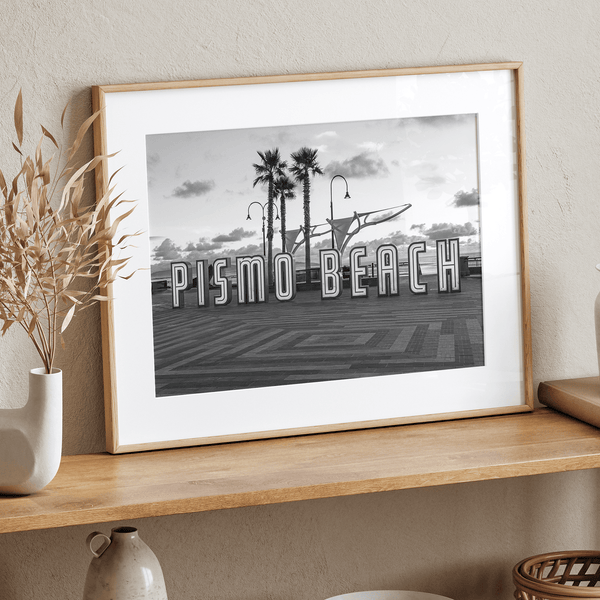 Black and white photo of the Pismo Beach street sign with palm trees and boardwalk – fine art coastal print