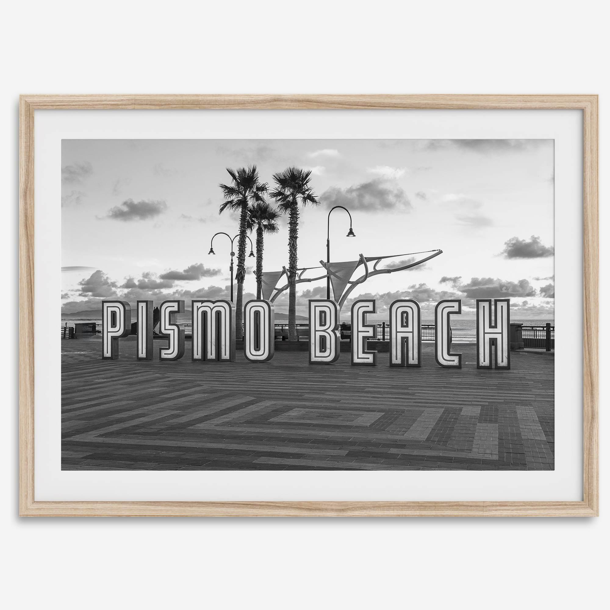 Black and white photo of the Pismo Beach street sign with palm trees and boardwalk – fine art coastal print