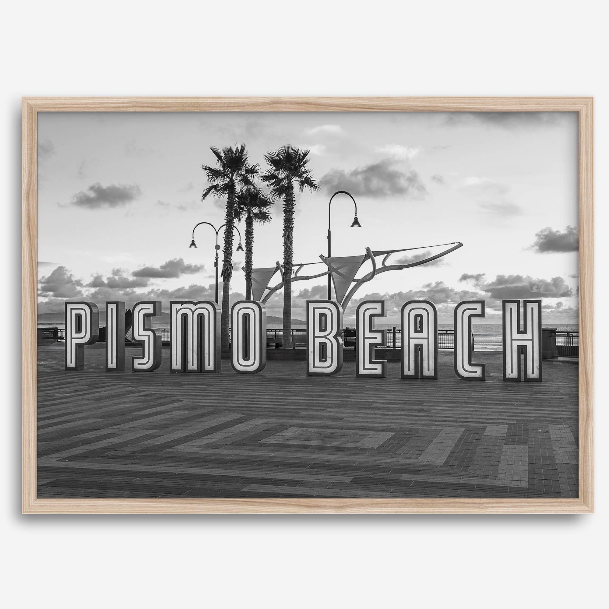 Black and white photo of the Pismo Beach street sign with palm trees and boardwalk – fine art coastal print