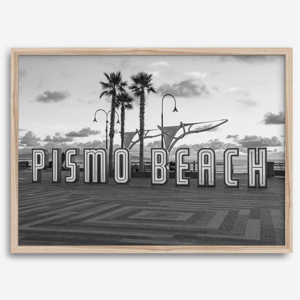 Black and white photo of the Pismo Beach street sign with palm trees and boardwalk – fine art coastal print