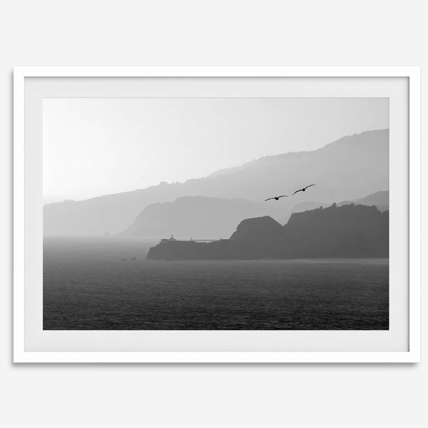 A black and white coastal wall art that showcases two Pelicans flying over the Pacific Ocean near the Golden Gate Bridge toward the layered mountains in the sunset.