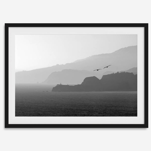 A black and white coastal wall art that showcases two Pelicans flying over the Pacific Ocean near the Golden Gate Bridge toward the layered mountains in the sunset.
