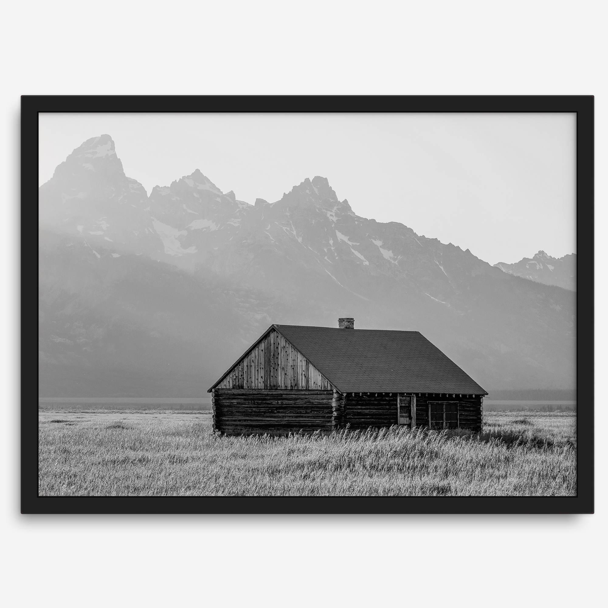 Step into Grand Teton National Park with this fine art black and white mountain print. This western landscape photo showcases a century-old rustic hut at the foot of the snowy, pointy Teton mountains.