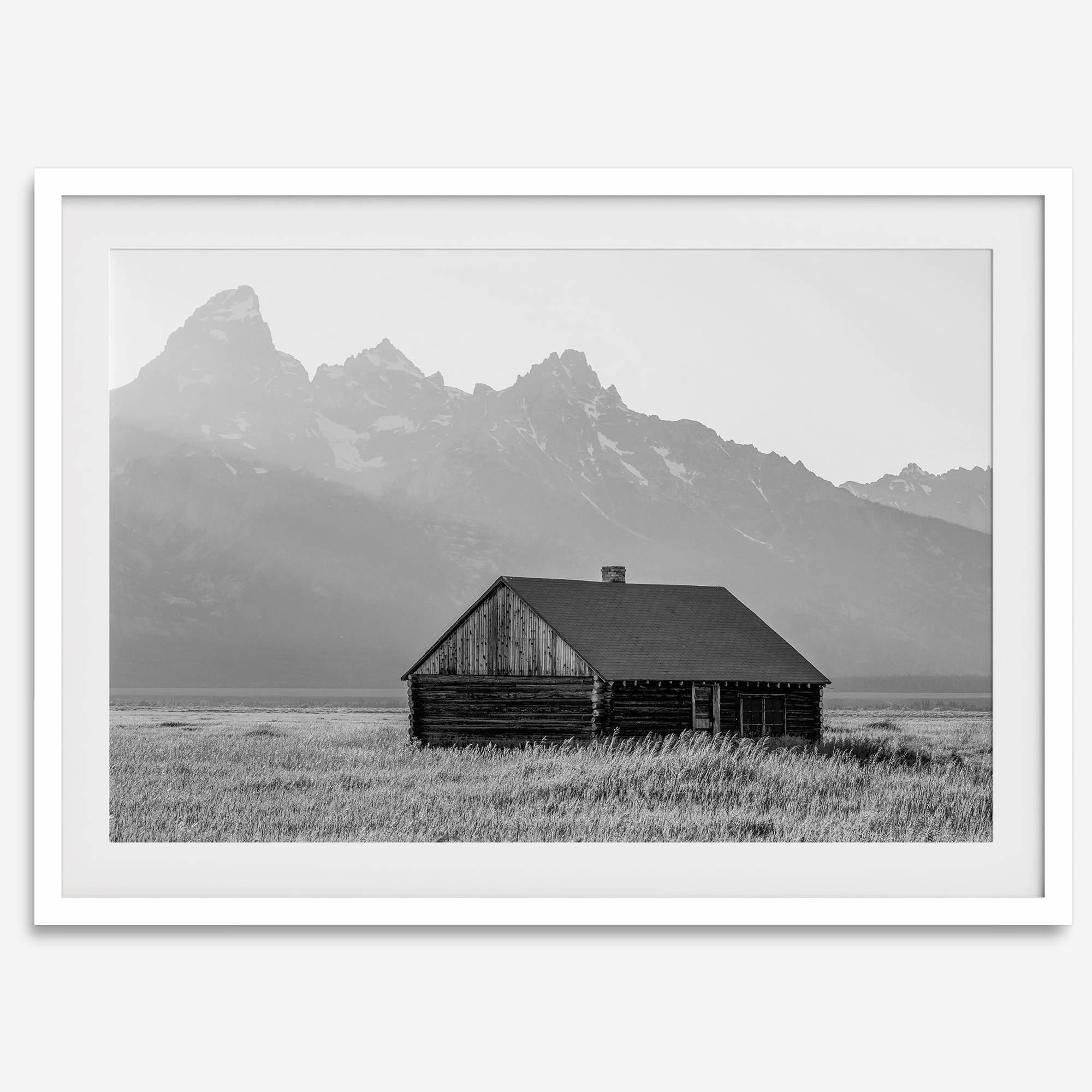 Step into Grand Teton National Park with this fine art black and white mountain print. This western landscape photo showcases a century-old rustic hut at the foot of the snowy, pointy Teton mountains.