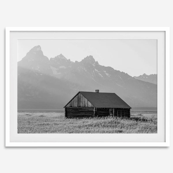 Step into Grand Teton National Park with this fine art black and white mountain print. This western landscape photo showcases a century-old rustic hut at the foot of the snowy, pointy Teton mountains.