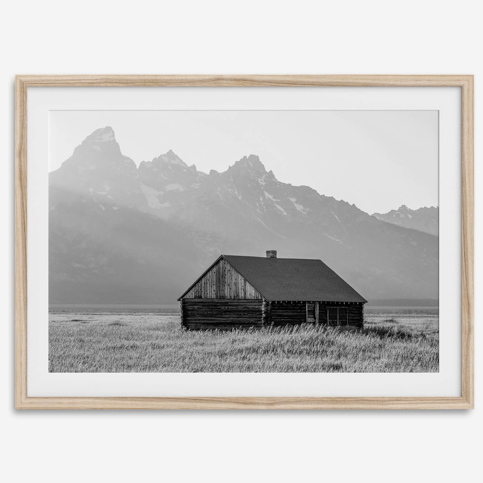 Step into Grand Teton National Park with this fine art black and white mountain print. This western landscape photo showcases a century-old rustic hut at the foot of the snowy, pointy Teton mountains.