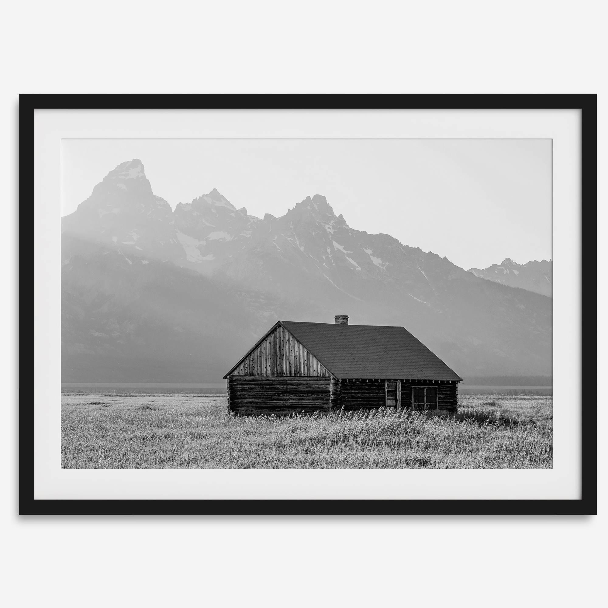 Step into Grand Teton National Park with this fine art black and white mountain print. This western landscape photo showcases a century-old rustic hut at the foot of the snowy, pointy Teton mountains.