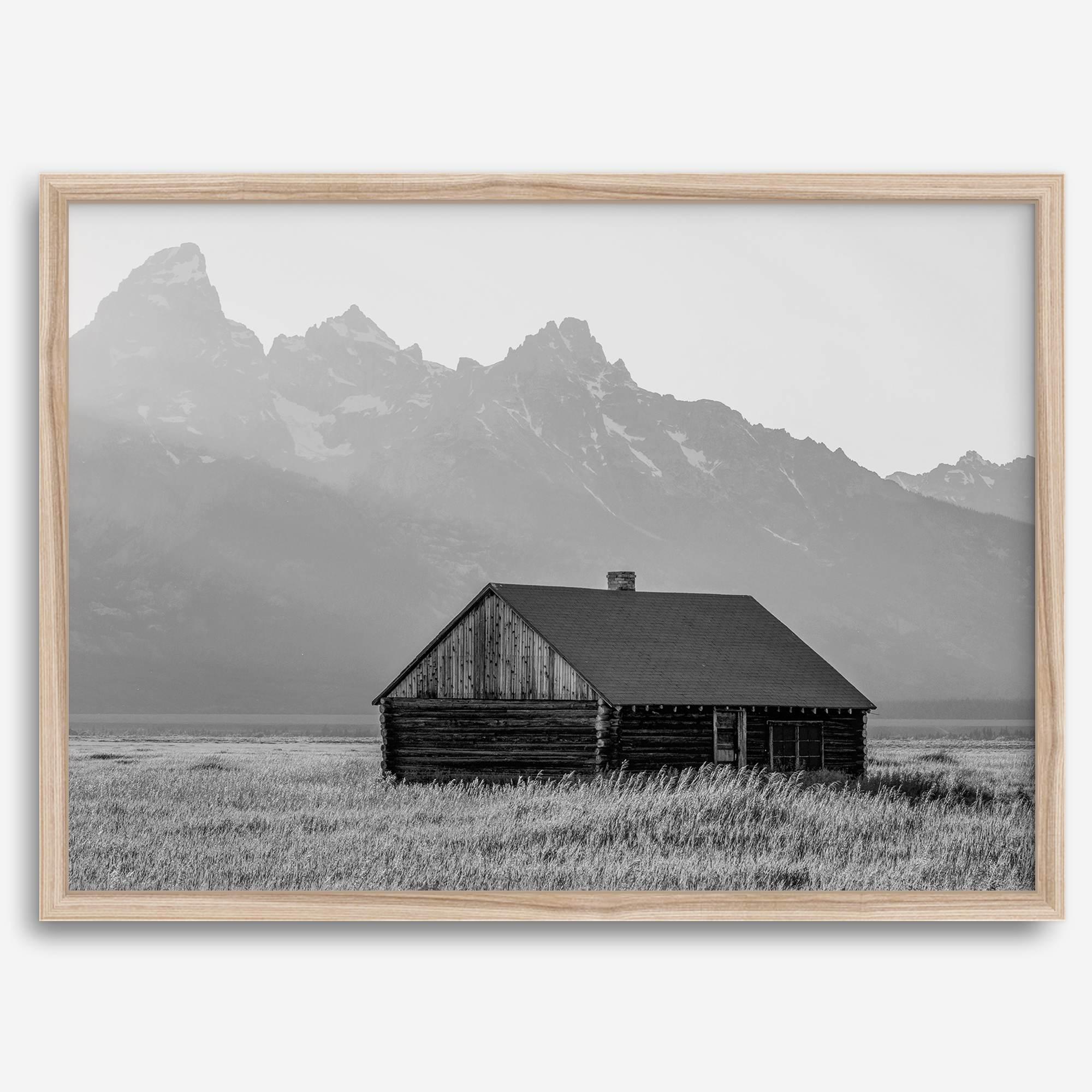 Step into Grand Teton National Park with this fine art black and white mountain print. This western landscape photo showcases a century-old rustic hut at the foot of the snowy, pointy Teton mountains.