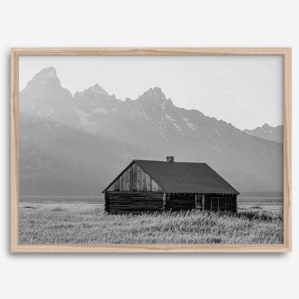 Step into Grand Teton National Park with this fine art black and white mountain print. This western landscape photo showcases a century-old rustic hut at the foot of the snowy, pointy Teton mountains.