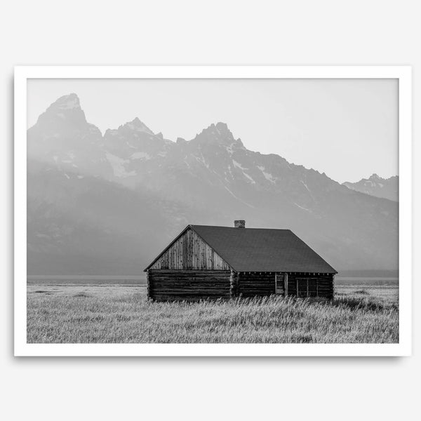 Step into Grand Teton National Park with this fine art black and white mountain print. This western landscape photo showcases a century-old rustic hut at the foot of the snowy, pointy Teton mountains.