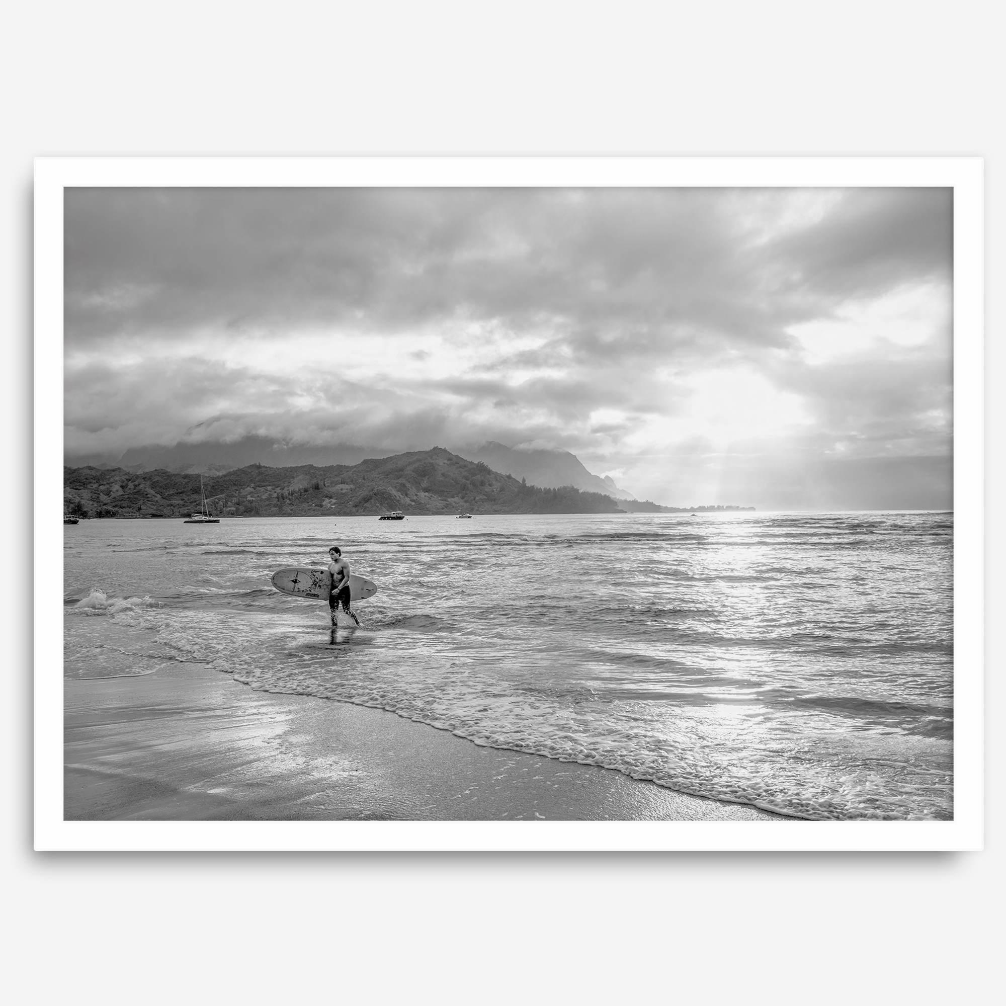 Surfer Wall Art featuring a lone surfer emerging from the ocean at Hanalei Bay in black-and-white photography.