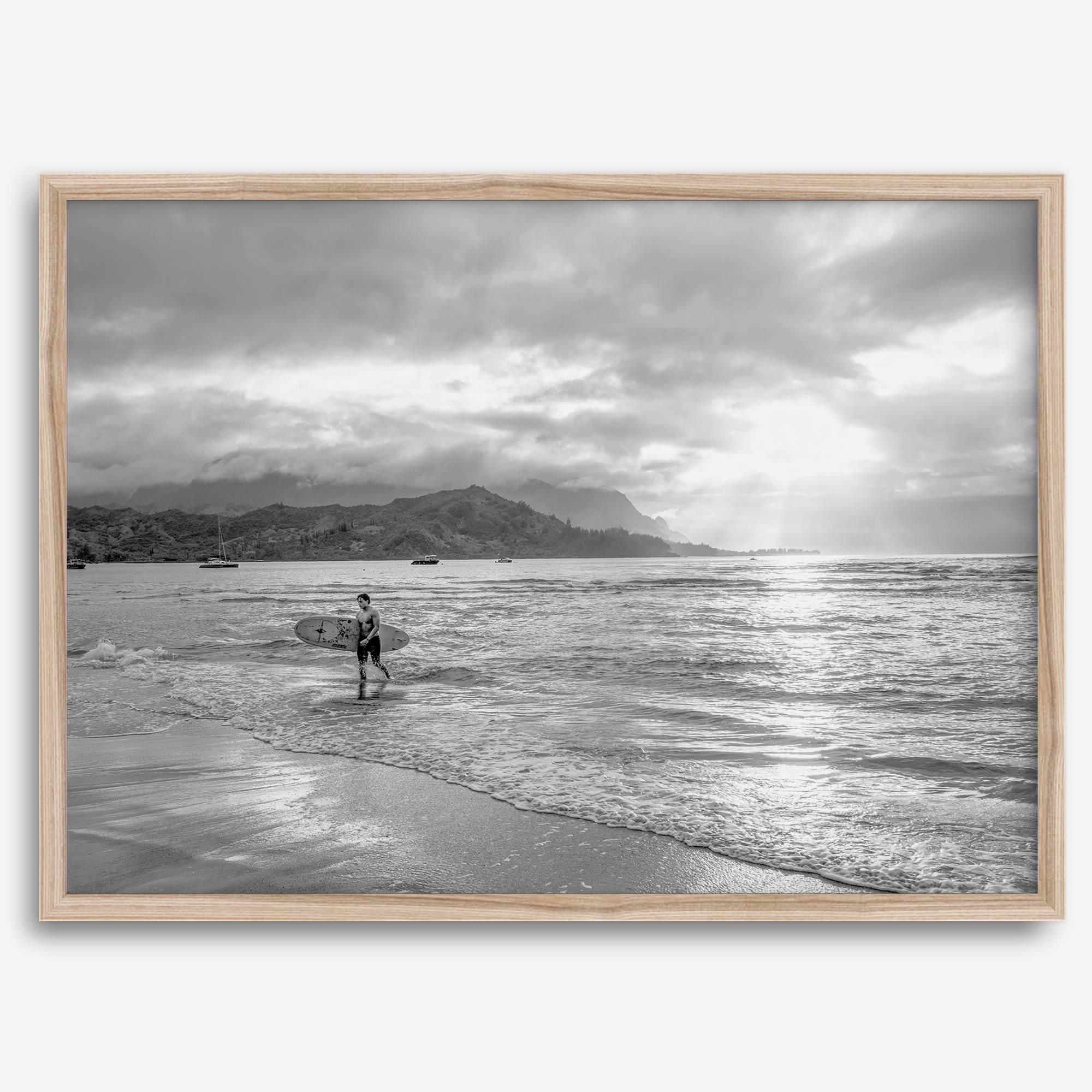 Surfer Wall Art featuring a lone surfer emerging from the ocean at Hanalei Bay in black-and-white photography.