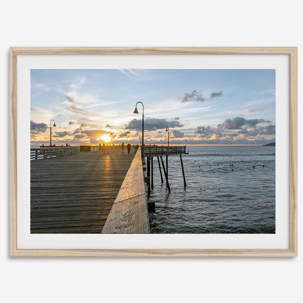 A fine art ocean sunset print featuring Pismo Beach Pier in Sunset with the surfers in the ocean and people enjoying a stroll on the pier.