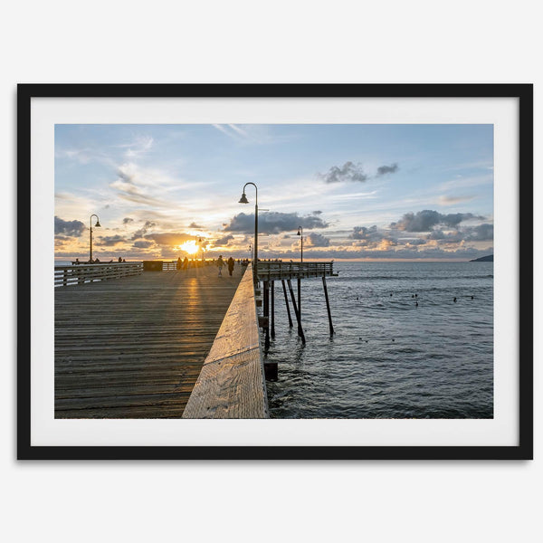 A fine art ocean sunset print featuring Pismo Beach Pier in Sunset with the surfers in the ocean and people enjoying a stroll on the pier.