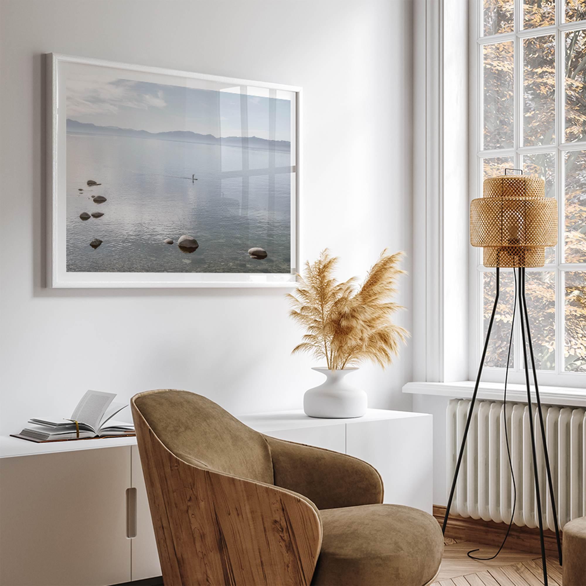 Fine art photography print of Lake Tahoe featuring a serene blue water surrounded by Pacific Northwest mountains, with a lone stand-up paddle silhouette on the lake.
