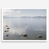 Fine art photography print of Lake Tahoe featuring a serene blue water surrounded by Pacific Northwest mountains, with a lone stand-up paddle silhouette on the lake.