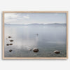 Fine art photography print of Lake Tahoe featuring a serene blue water surrounded by Pacific Northwest mountains, with a lone stand-up paddle silhouette on the lake.