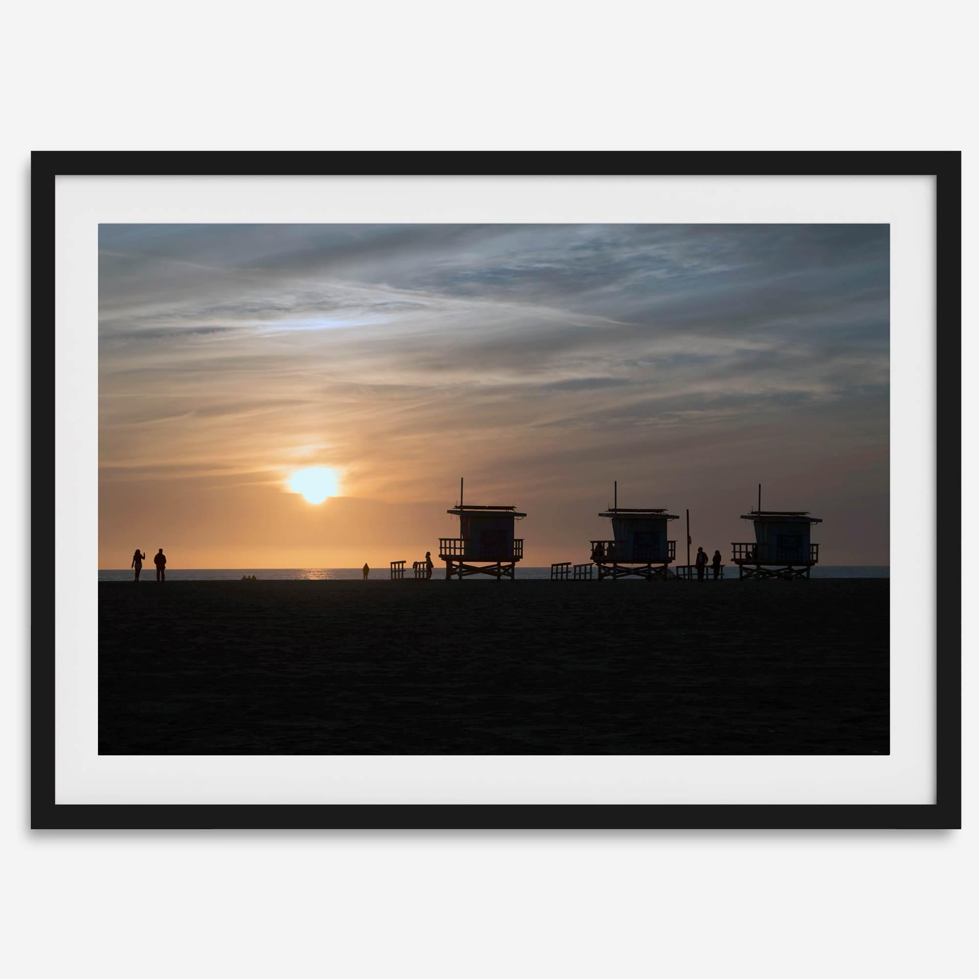 Step into Venice Beach with our fine art beach sunset framed or unframed print. The print showcases the beach in sunset with the silhouettes of the famous lifeguard towers and people in the sunset.