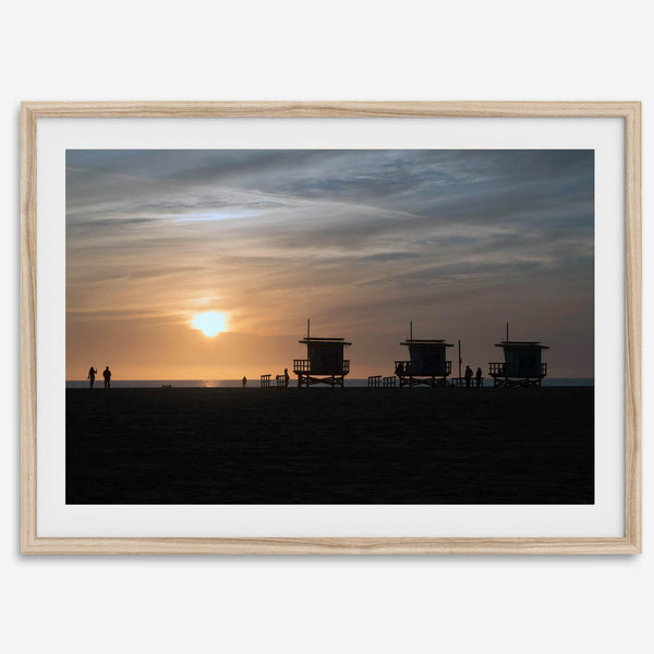 Step into Venice Beach with our fine art beach sunset framed or unframed print. The print showcases the beach in sunset with the silhouettes of the famous lifeguard towers and people in the sunset.