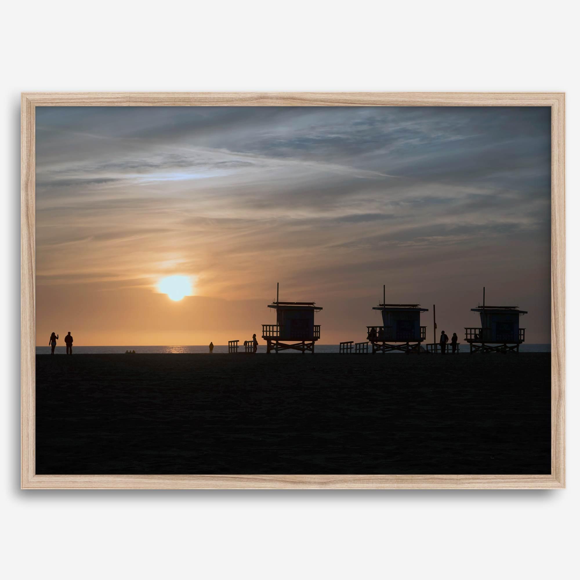 Step into Venice Beach with our fine art beach sunset framed or unframed print. The print showcases the beach in sunset with the silhouettes of the famous lifeguard towers and people in the sunset.