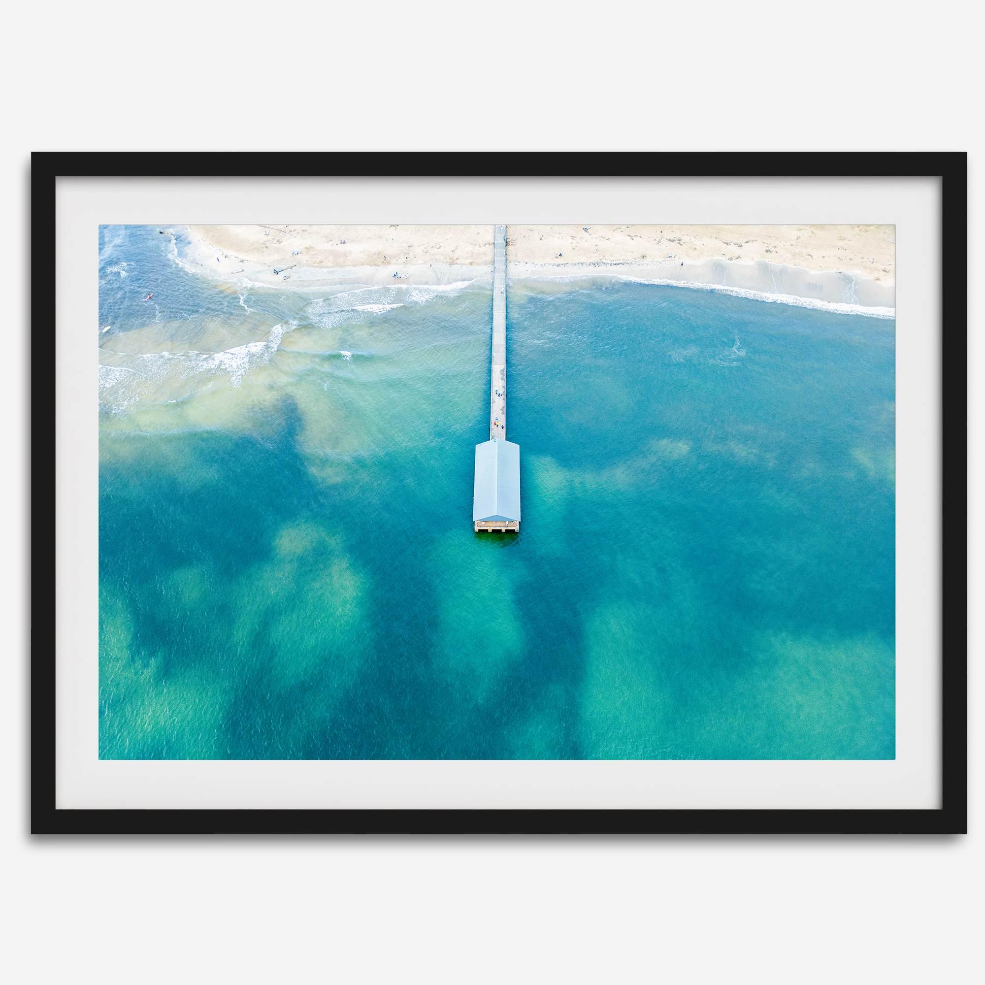 Drone photo of a pier extending into clear blue ocean at Hanalei Beach, Kauai, Hawaii.