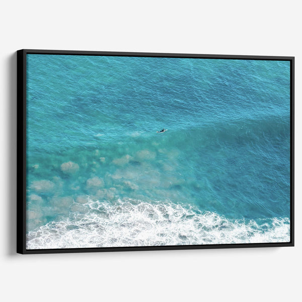 Aerial ocean canvas print showing a lone surfer paddling through turquoise waves with white surf along the beach shoreline