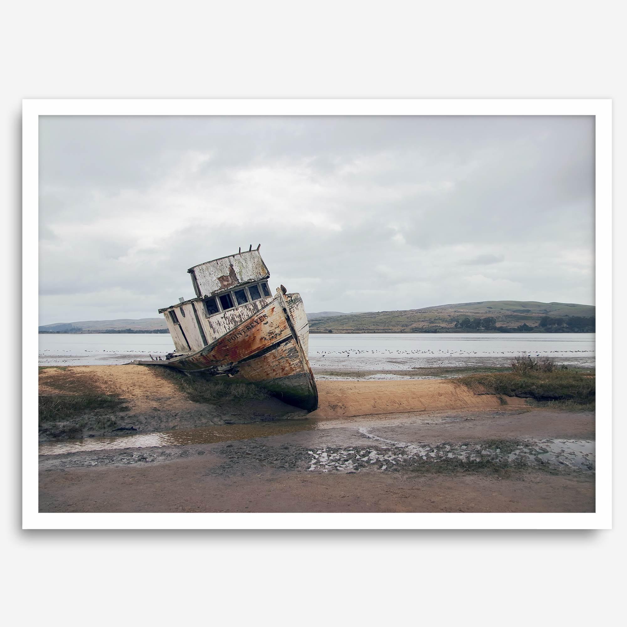 Weathered shipwreck resting on a quiet coastal shore, surrounded by marshland and a moody, overcast sky.