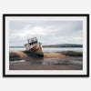 Weathered shipwreck resting on a quiet coastal shore, surrounded by marshland and a moody, overcast sky.