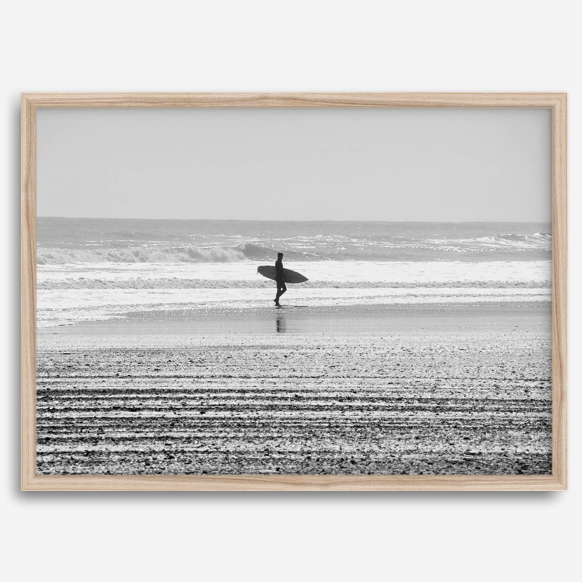 Black and white surfer photography showing a lone surfer on the beach, with waves in the background, capturing minimalist coastal beauty.