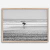 Black and white surfer photography showing a lone surfer on the beach, with waves in the background, capturing minimalist coastal beauty.